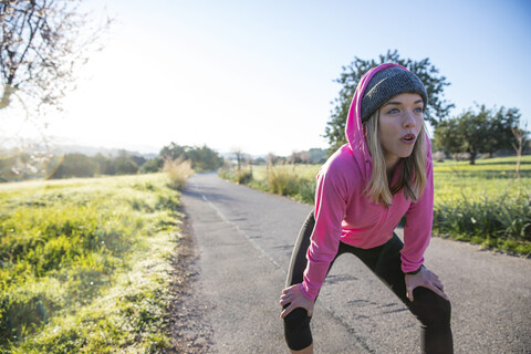 Junge Frau im Freien, die eine Pause vom Sport macht, Hände auf den Knien, lizenzfreies Stockfoto