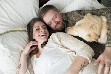 Pregnant woman lying with partner on bed, dog lying on bed beside them, elevated view - CUF02549