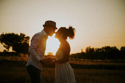 Heterosexuelles Paar in einem Feld bei Sonnenuntergang, Hände haltend, von Angesicht zu Angesicht, lizenzfreies Stockfoto