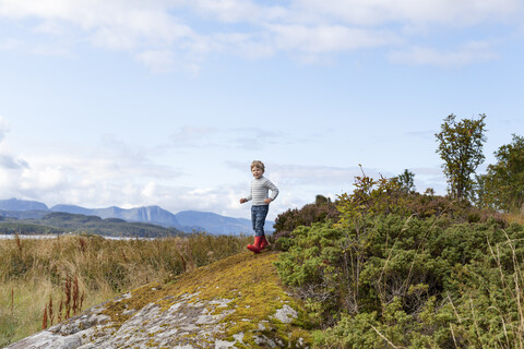 Junge spielt auf einem Felsen am Fjord, Aure, More og Romsdal, Norwegen, lizenzfreies Stockfoto