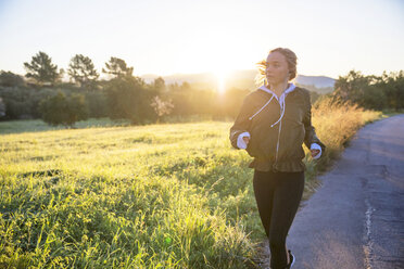 Young woman running along rural road - CUF02564