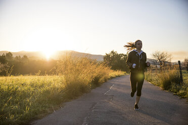 Young woman running along rural road - CUF02565