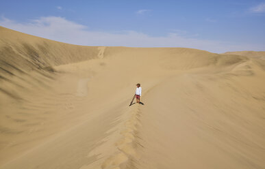 Boy with sandboard looking out over sand dunes, Ica, Peru - CUF02595