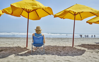 Rear view of female tourist sitting under beach umbrella, Camana, Arequipa, Peru - CUF02597