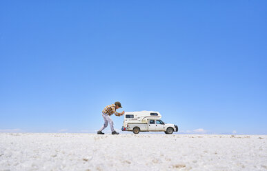 Falschperspektivisches Bild eines Jungen auf einer Salzwiese, der so tut, als würde er ein Freizeitfahrzeug schieben, Fahrzeug im Hintergrund, Salar de Uyuni, Uyuni, Oruro, Bolivien, Südamerika - CUF02607