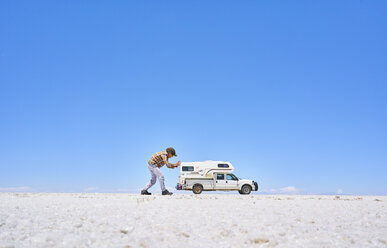 False perspective image of boy on salt flats, pretending to push recreational vehicle, vehicle in background, Salar de Uyuni, Uyuni, Oruro, Bolivia, South America - CUF02607