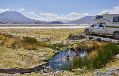 Zwei Jungen spielen im Wasserbecken neben einem geparkten Wohnmobil, Salar de Chiguana, Chiguana, Potosi, Bolivien, Südamerika - CUF02608