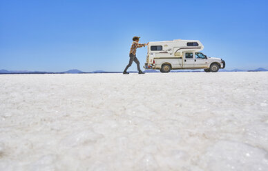 False perspective image of boy on salt flats, pretending to push recreational vehicle, vehicle in background, Salar de Uyuni, Uyuni, Oruro, Bolivia, South America - CUF02609