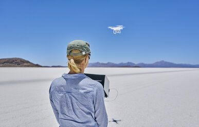 Woman on salt flats, flying drone, rear view, Salar de Uyuni, Uyuni, Oruro, Bolivia, South America - CUF02619