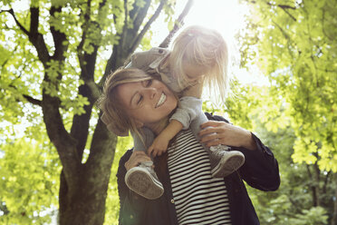 Mother giving toddler daughter shoulder carry in sunlit park - CUF02663