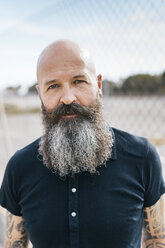 Porträt eines reifen männlichen Hipsters mit grauem Bart vor einem Drahtzaun - CUF02671