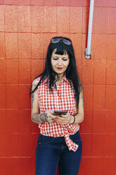 Älterer weiblicher Hipster lehnt an einer roten Wand und schaut auf sein Smartphone - CUF02682