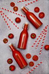 Homemade tomato juice in swing top bottles, straws and tomatoes on grey ground - RTBF01266