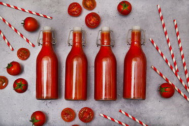 Row of four swing top bottle of homemade tomato juice, straws and tomatoes on grey ground - RTBF01268