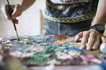 Männlicher Künstler mischt Ölfarbe auf einer Palette in einem Künstleratelier, Nahaufnahme der Hände - CUF02724