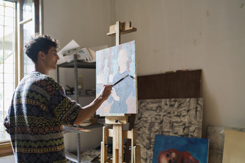 Männlicher Künstler, der an einer Staffelei im Künstleratelier eine Leinwand bemalt, lizenzfreies Stockfoto