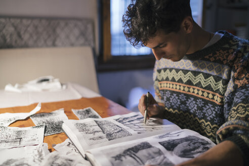 Männlicher Künstler zeichnet in einem Skizzenbuch am Schreibtisch in einem Künstleratelier - CUF02729