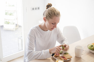 Young woman peeling kiwi fruit at breakfast table - CUF02749