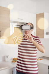 Mature man looking through virtual reality headset in kitchen - CUF02751