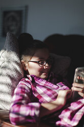 Girl relaxing on sofa, looking at smartphone - CUF02791