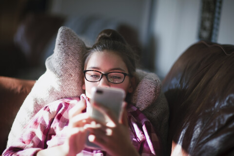 Mädchen entspannt sich auf dem Sofa und schaut auf ihr Smartphone, lizenzfreies Stockfoto