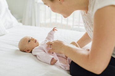 Young woman dressing baby daughter on bed - CUF02854