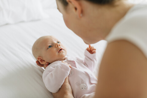 Junge Frau wiegt ihre kleine Tochter im Bett, Blick über die Schulter, lizenzfreies Stockfoto