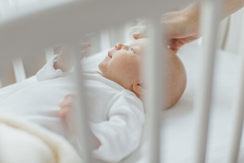 Ein kleines Mädchen liegt in einem Kinderbett, die Hand der Mutter beruhigt den Kopf, lizenzfreies Stockfoto