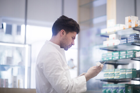 Junger männlicher Apotheker, der in einer Apotheke eine Medikamentenpackung liest, lizenzfreies Stockfoto