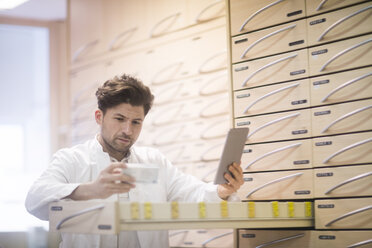 Junger männlicher Apotheker, der ein digitales Tablet benutzt und eine Medikamentenpackung in einer Apotheke liest - CUF02867