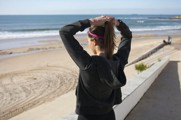 Rear view of young woman at beach tying hair in ponytail, Carcavelos, Lisboa, Portugal, Europe - CUF02887