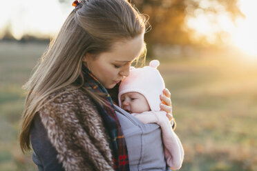 Mother and baby daughter outdoors, mother carrying baby in baby sling - CUF02891