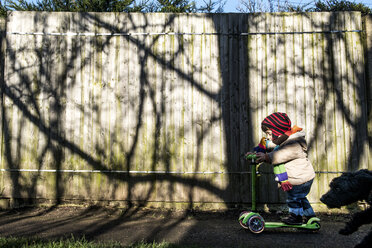 Männliches Kleinkind auf einem Tretroller in einem sonnenbeschienenen Park - CUF02899