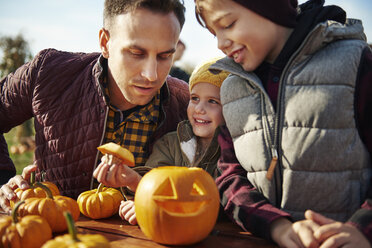 Mann mit Sohn und Tochter betrachten einen geschnitzten Halloween-Kürbis im Kürbisfeld - CUF02913