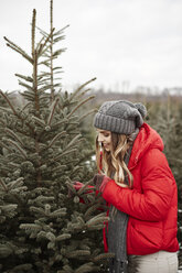 Junge Frau betrachtet Tannennadeln beim Einkaufen eines Weihnachtsbaums im Wald - CUF02923