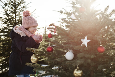 Mädchen betrachtet Christbaumkugeln auf einem Waldweihnachtsbaum - CUF02925