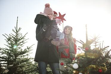 Girl and parents placing star on forest christmas tree - CUF02927