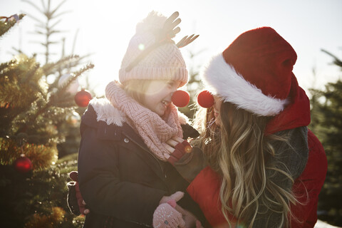 Mädchen und Mutter im Weihnachtsbaumwald mit roten Nasen, lizenzfreies Stockfoto