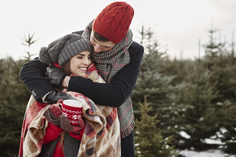 Romantisches junges Paar im Weihnachtsbaumwald in Decke eingewickelt, lizenzfreies Stockfoto