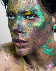 Studioporträt einer blauäugigen jungen Frau mit glitzerndem mehrfarbigem Puder im Gesicht - CUF02952
