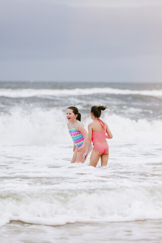 Zwei Mädchen stehen in den Wellen des Ozeans, Dauphin Island, Alabama, USA, lizenzfreies Stockfoto