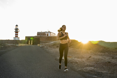 Junge Läuferin läuft bei Sonnenuntergang eine Landstraße entlang, Las Palmas, Kanarische Inseln, Spanien, lizenzfreies Stockfoto