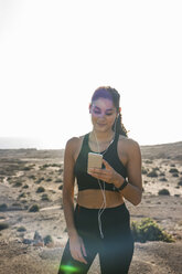 Junge Läuferin, die in einer trockenen Küstenlandschaft auf ihr Smartphone schaut, Las Palmas, Kanarische Inseln, Spanien - CUF02976