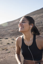 Glückliche junge Läuferin, die in einer trockenen Landschaft Kopfhörer hört - CUF02977
