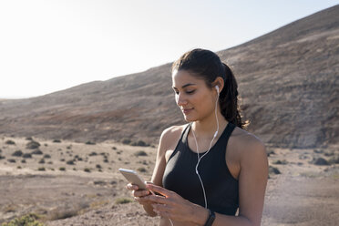 Junge Läuferin schaut in trockener Landschaft auf ihr Smartphone, Las Palmas, Kanarische Inseln, Spanien - CUF02978