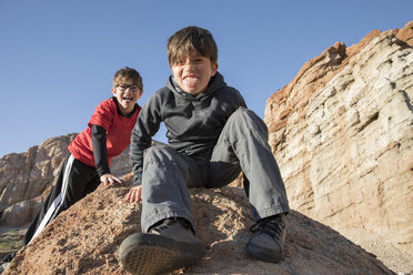 Porträt von Jungen, die auf einem Felsen sitzen und in die Kamera schauen, mit herausgestreckter Zunge, Lone Pine, Kalifornien, USA - CUF02988