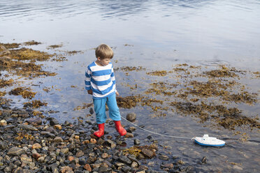 Junge am Fjordufer, der mit einem Spielzeugboot spielt, Aure, More og Romsdal, Norwegen - CUF03017