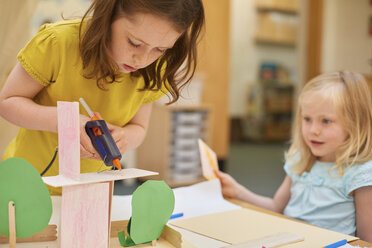 Primary schoolgirls making cardboard model at classroom desk - CUF03040