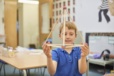 Grundschüler hält Plastikstrohpyramide im Klassenzimmer hoch - CUF03044