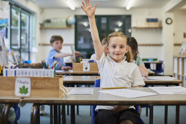 Schoolgirl with hand raised in classroom at primary school - CUF03064